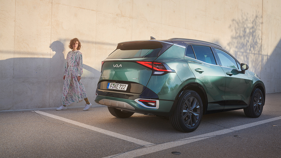 Frau läuft an grünem Sportage vorbei und dreht sich danach um